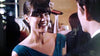 A woman in a teal dress smiles while discussing The Good Doctor (2011) DVD with a man at a social event, surrounded by other guests and warm lighting in the background.