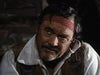 A bearded man in a red headband and rustic attire gazes forward in dim light, evoking the adventurous Native American spirit of classic frontier films as seen in Grayeagle (1977) DVD.