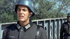 A man in a dark military uniform and helmet stands near a bridge, capturing the tense WWII action of "Legion of No Return (1969)" DVD; another similarly dressed figure and trees appear in the background.