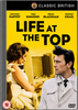 DVD cover for Life At The Top DVD (1965), the acclaimed sequel to Room at the Top, featuring a woman seated at a vanity and a man in a trench coat, set against a bold yellow background with the film’s title in large black letters. Cast names appear across the top of this Laurence Harvey movie collectible.