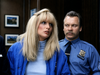 A woman with long blonde hair in a blue jacket stands beside a police officer in uniform, inside a room adorned with framed photos—a scene that echoes the cult horror classic Maniac Cop (1988), now available on DVD for rare movie enthusiasts.