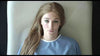 A woman in a light blue hospital gown with long light brown hair lies on a white surface, gazing at the camera—a scene evocative of Nelly (2016) DVD, a rare biographical drama.