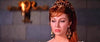A woman with elegant red hair, gold headpiece, and black-and-gold earrings gazes thoughtfully by a stone wall—capturing the timeless allure found in "Goliath and the Dragon (1960)" DVD.