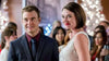 A man in a suit and a woman in a sleeveless dress smile at a festive indoor event, with blurred people and decorated trees in the background, capturing the joyful spirit of “On the Twelfth Day of Christmas (2015) DVD,” an ideal choice for fans of holiday romance movies.