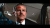 A man with neatly combed hair and a mustache, dressed in a suit, bears a red mark on his forehead and gazes off-camera with a stern expression. Evoking the stylish tension of a neo-noir thriller, the scene recalls the gritty atmosphere found in rare hard-to-find movies such as Point Blank (1967), now available on DVD. A blurred vehicle can be seen in the background.