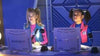 Two young girls in colorful outfits sit at computer stations with microphones, focused on their screens in a futuristic, blue-lit room—evoking the high-tech vibe of a Disney Channel original movie or the sci-fi excitement found in Zenon Girl of the 21st Century (1999) DVD.