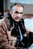 A man with gray hair and a mustache wears a brown shearling coat over a suit and tie, sitting indoors and looking seriously toward the camera, evoking the timeless style of classic films such as Meteor (1979) starring Sean Connery and Natalie Wood, now available on DVD.