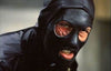 A person wearing a black leather mask with holes for the mouth and one eye, their visible eye appearing severely scarred or injured while baring their teeth in a grimace—a haunting image reminiscent of characters featured in the cult classic “Death Race 2000 (1975)” DVD.