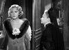 A woman in a light dress with a fur collar and flower stands beside an older woman in dark, formal attire and a veil, indoors—a classic black-and-white film scene evocative of William Wyler’s masterful direction in “Dodsworth (1936)”, now available on DVD for collectors of rare movies.