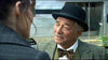 An older man in a bowler hat, bow tie, and plaid jacket smiles gently while speaking to a woman whose back is to the camera—capturing the timeless holiday spirit found in “When Angels Come To Town (2004)” on DVD.
