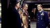 Three men stand indoors: one wears a hat and coat, another has on a shearling jacket, and the third is dressed in an ornate blue military uniform, speaking with intensity—reminiscent of a suspenseful scene from *Meteor (1979)* DVD, the rare classic movie featuring stars like Sean Connery and Natalie Wood.