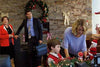 A woman decorates a table with Christmas items as a boy watches, while a man with a briefcase and an older woman stand close by. The room is festive with wreaths, bows, and holiday decorations—capturing the heartwarming atmosphere of “A Gift Wrapped Christmas (2015)” DVD, an enchanting film perfect for any cherished Christmas romance collection.
