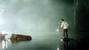 A man in a white shirt holds a flashlight and red lantern while standing on a rock amid foggy water and logs at night, evoking a scene from the Rogue (2007) DVD.