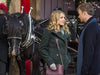 A woman and a man stand facing each other in conversation, both dressed in jackets, with a black horse harnessed to a carriage behind them—evoking the enchanting atmosphere featured in “On the Twelfth Day of Christmas (2015) DVD.”.