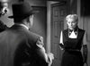 A woman in a dark dress holds a gun and confronts a man in a suit and hat inside a room, creating a tense scene evocative of vintage noir crime thrillers, reminiscent of the classic film “Kiss Tomorrow Goodbye (1950)” available on DVD.