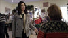 At a holiday gathering that glows with the nostalgic warmth of a classic film, a woman in a gray coat smiles and gestures while chatting with another guest in a festive sweater—capturing the spirit and joy reminiscent of scenes from Magic Stocking (2015), surrounded by twinkling decorations and laughter that echoes through the room.
