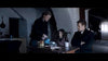 A woman pours tea for a young girl and a man in a shadowy room crowded with household items, creating the eerie folk horror mood of "Post Mortem (2020)"—now available on DVD. The man sits with arms crossed, watching the woman closely.