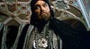 A man in ornate, dark medieval robes and jeweled necklaces stands under a colorful ceiling with a stern gaze—reminiscent of characters from 80s fantasy like "Sinbad of the 7 Seas (1989)" on DVD.