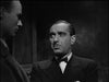 A man in a suit and bow tie stands indoors, looking serious against a shadowy background that channels the vintage horror vibe of The Ghoul (1933) DVD.