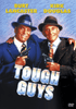 Two smiling men in suits and hats hold guns, standing close together. The text above them reads "Burt Lancaster and Kirk Douglas," stars of the classic 1986 train robbery movie. Bold title text below says "Tough Guys." A "Tough Guys DVD (1986)" logo appears in the bottom right corner.