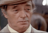 An older man wearing a brown flat cap and beige coat looks slightly off-camera with a serious expression, reminiscent of a character from a classic film like The Amsterdam Kill (1977) on DVD.
