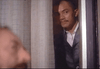 A man with a mustache peers seriously through a partially open door as another man’s blurred profile appears in the foreground, capturing the tense atmosphere of a classic crime thriller in “The Amsterdam Kill DVD (1977).”.