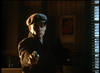 A man in a dark coat and flat cap stands indoors, gun pointed forward as light streams through blinds—a gritty scene reminiscent of rare classics like Killer Instinct DVD (1992).