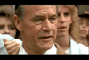 A close-up of an older man with gray hair and blue eyes standing among a group of people outdoors, their blurred faces evoking the dramatic atmosphere found in classic martial arts films like “Only the Strong (1993)” on DVD.