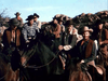 A group of cowboys in western attire ride horses across a rocky desert under clear skies, evoking classic film scenes like those in "Outlaw Women (1952) DVD.
