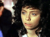 A person with curly dark hair and blue eyes looks to the side with a serious expression, as if reflecting on "A Deadly Silence (1989)" DVD; the background is blurred.