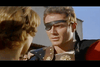 A man in Roman armor and a leather eyepatch faces someone with light brown hair, channeling vintage movie vibes like Amazons of Rome (1961) DVD, with a clear blue sky and building in the background.