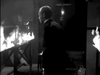A man in a suit stands in a dimly lit room, facing a table ablaze, while a lantern and assorted objects cast eerie shadows in the background—evoking the tense, dramatic atmosphere of vintage classics such as *The Snake Woman* DVD, and capturing the suspenseful mood often found in gothic horror films.
