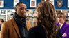 Three people interact in front of colorful bookshelves—a man in a brown coat and scarf faces a woman with wavy hair, while another woman in a purple blazer looks on—capturing the romance of "Game of Love (2023)" on DVD.