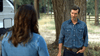 A man in a denim shirt and belt buckle stands by a tree, facing a woman in a denim jacket with long brown hair. A white trailer sits behind them—an evocative scene from "The Real West (2024)" DVD.