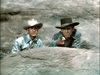 Experience the suspense as two men in cowboy hats take cover behind a rock—one aiming his gun, the other on watch—in The Nevadan (1950) DVD, a rare classic perfect for your movie collection.