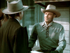Two men in cowboy hats talk outside a wooden building—one in a gray laced-collar shirt, the other in a dark suit—capturing the classic Western feel of "The Nevadan (1950)" DVD.