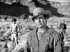 A man in a fringed jacket and cowboy hat stands in the desert, with two others in Western wear nearby among shrubs and rocky hills—evoking scenes from The Yellow Tomahawk (1954) DVD.
