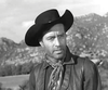 A man in a wide-brimmed black cowboy hat, leather vest, and neckerchief stands before rocky hills in this black and white photo—evoking classic Westerns like the rare Gun Duel at Durango (1957) DVD.