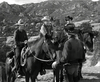 Four cowboys, three on horseback and one standing, talk on a rugged trail with rocky hills behind them in a black-and-white scene from the rare film "Gun Duel at Durango" (1957) DVD.