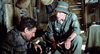 Two men in military uniforms sit in a dim hut—one crouched, one in a bucket hat and green uniform, talking seriously—in a gripping scene from Go Tell the Spartans (1978) DVD.