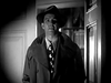 A man in a fedora, trench coat, and patterned tie stands in a shadowy doorway—classic film noir style—in "Apology for Murder (1945)" now on DVD, perfect for rare movie collectors.