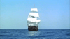 A large sailing ship with white sails sails on a calm blue sea under a clear sky, like a scene from the 1960 classic "Morgan The Pirate" DVD.