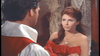 A woman with long brown hair in a red off-the-shoulder dress faces a man in white shirt and red vest, evoking pirate movie drama, indoors by a stone wall—just like scenes from the classic Morgan The Pirate DVD (1960).