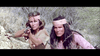 Two people in tan headbands crouch in dry brush. The person on the left aims a rifle, while the person on the right looks ahead intently. Both wear earth-toned clothing and appear focused and alert—an intense scene reminiscent of moments found in rare movies like Five Savage Men (1971) DVD.