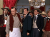 A group of men in Old West attire stands in an ornate room with red curtains and a chandelier—evoking the suspense of rare classics like The Man Behind the Gun (1953), available on DVD. One man in an apron leads as others watch intently.