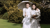Two women in vintage white dresses, one with a parasol, stroll across the grass in a scene reminiscent of 1923 London, evoking the atmosphere found in Mrs. Dalloway (1997) DVD.