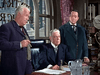 Three older men in suits gather around a desk in a formal office with large arched windows, creating a classic atmosphere reminiscent of "Carson City (1952)" on DVD. Two stand while one sits among papers and a glass pitcher, adding to the serious mood.