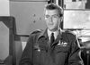 A man in military uniform with medals sits indoors, speaking and blinking, with a window and office furniture behind him. This black-and-white scene recalls the WWII drama of Raiders in the Sky (1953) DVD.