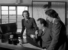 Four uniformed figures, three standing and one seated, gather around radio equipment and papers in a control room overlooking an airfield—capturing the classic WWII atmosphere of Raiders in the Sky (1953) DVD.