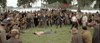 A shirtless man lies on grass, surrounded by a crowd in vintage attire, watching tensely—reminiscent of iconic scenes from classic films like the Hard Times (1975) DVD.
